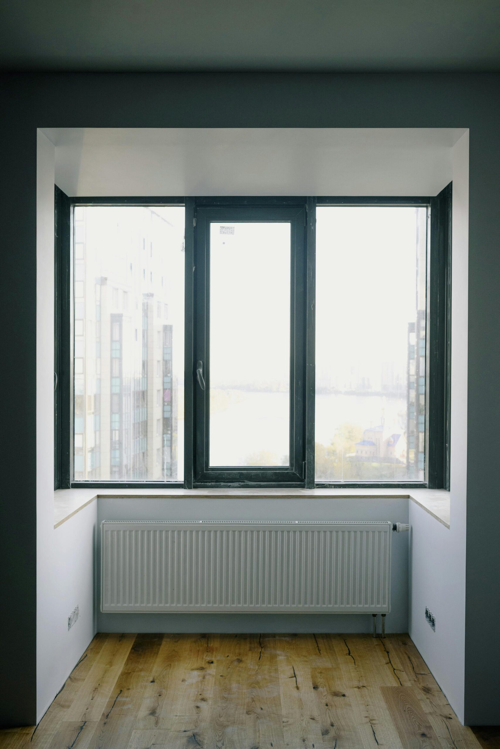 Wide transparent rectangular window and simple radiator in enclosed balcony with furniture in daytime